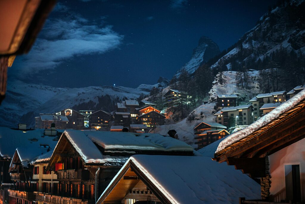 Scenic alpine village covered in snow, illuminated under a starry winter night sky.